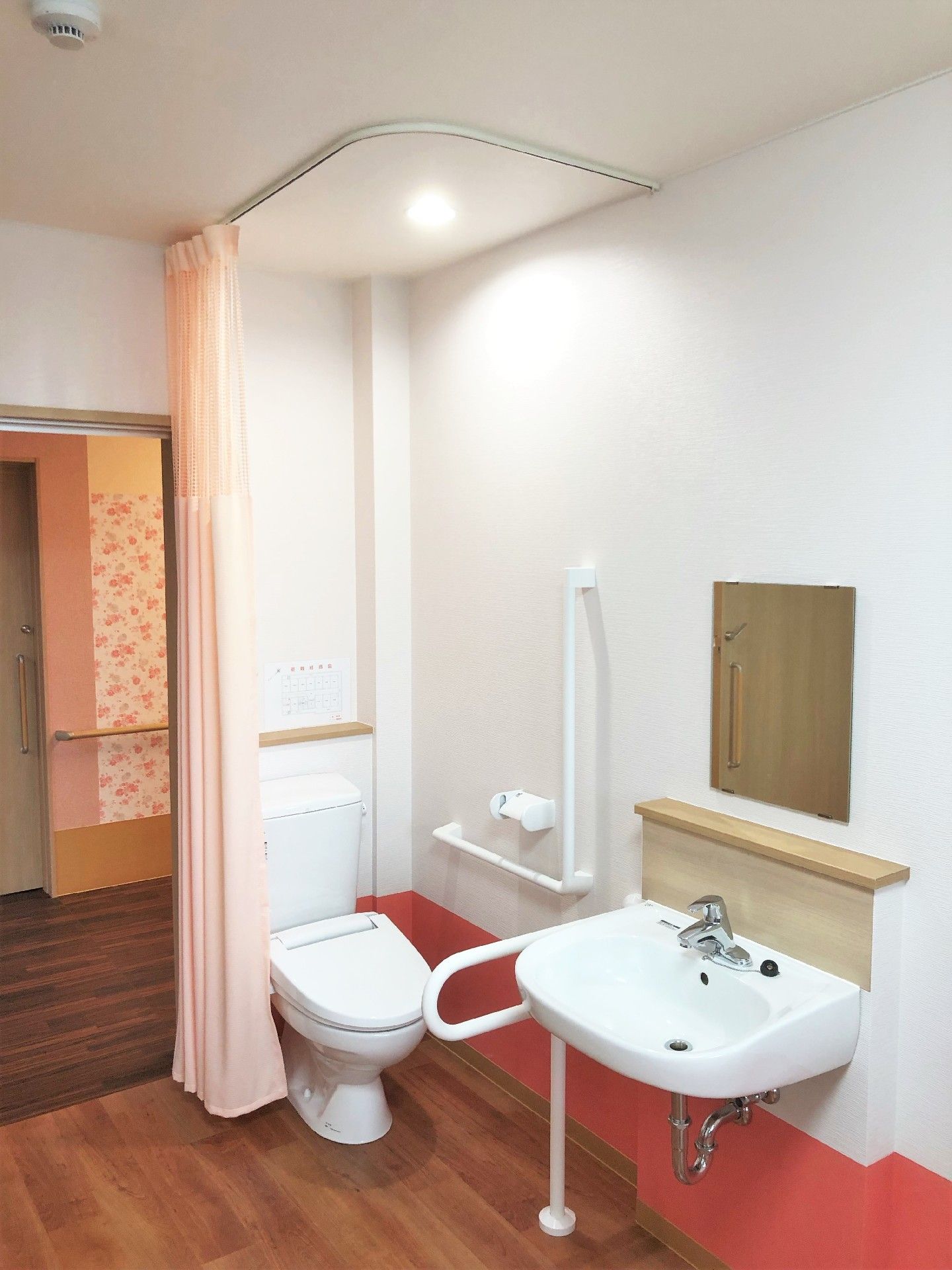 白と赤のラインが引かれた壁の居室。入り口側にはカーテンで仕切られたトイレがある。