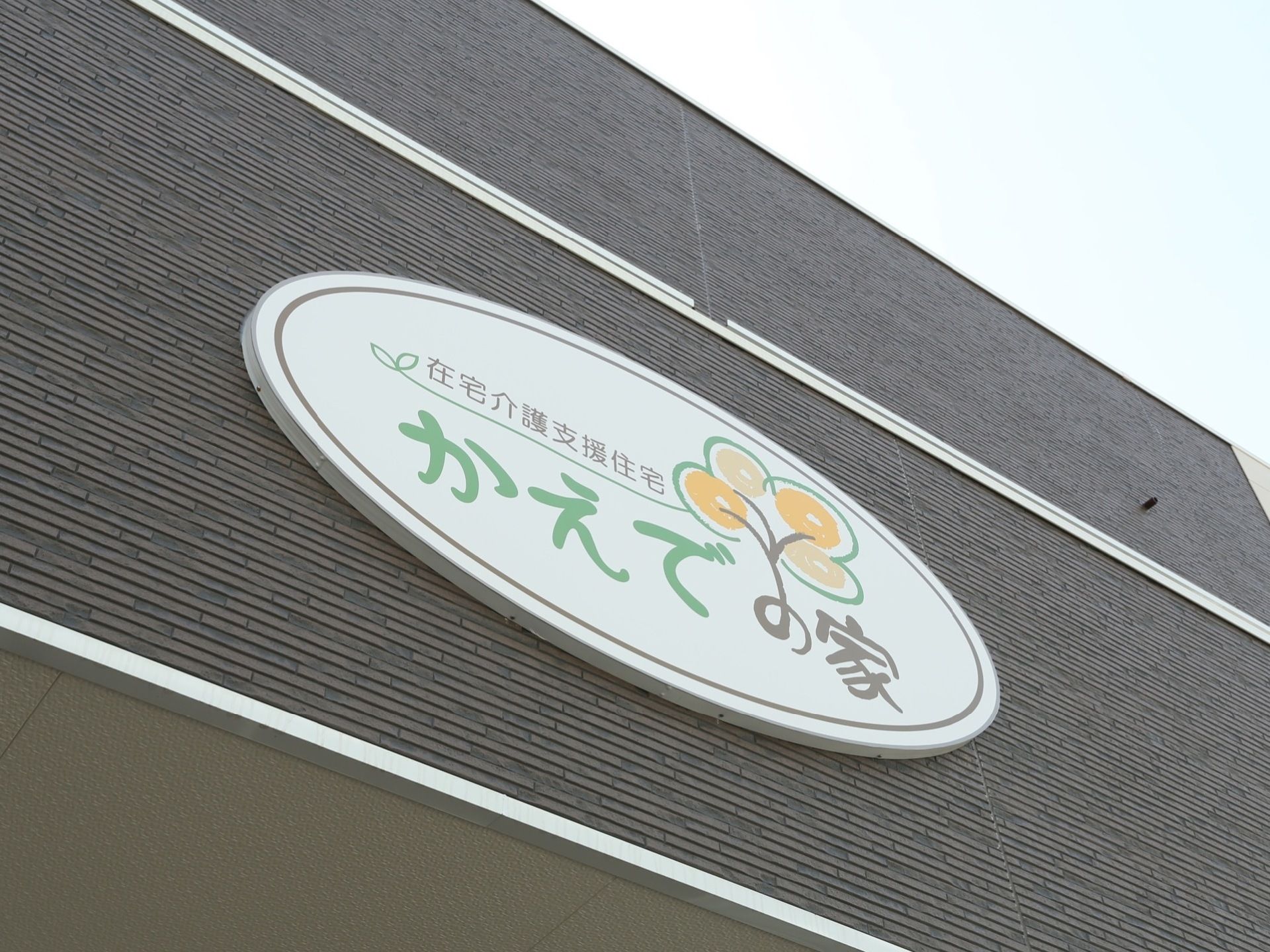 施設外壁に施設プレートが設置されている。白い楕円形のプレートに施設種別と施設名称が、デザイン文字でロゴマークとともに描かれている。