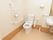 広いトイレスペースに、蓋がついていない洋式便器が据えてある。壁面には、ナースコールとＬ字型の手すりが設置されている。