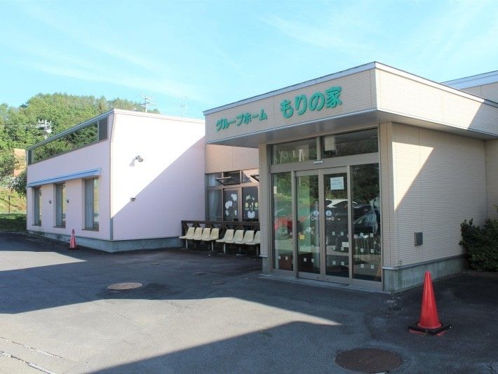 平屋建ての建物の周辺には緑が多くあり、屋外には椅子や駐車場も設置されている。