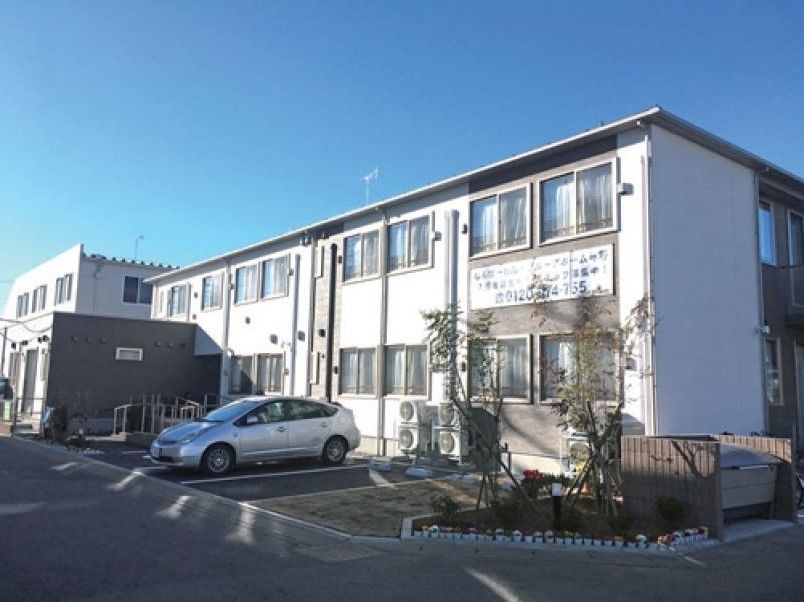 白を基調とした2階建ての建物の周りには自然が多く、玄関先にはスロープが付いている。