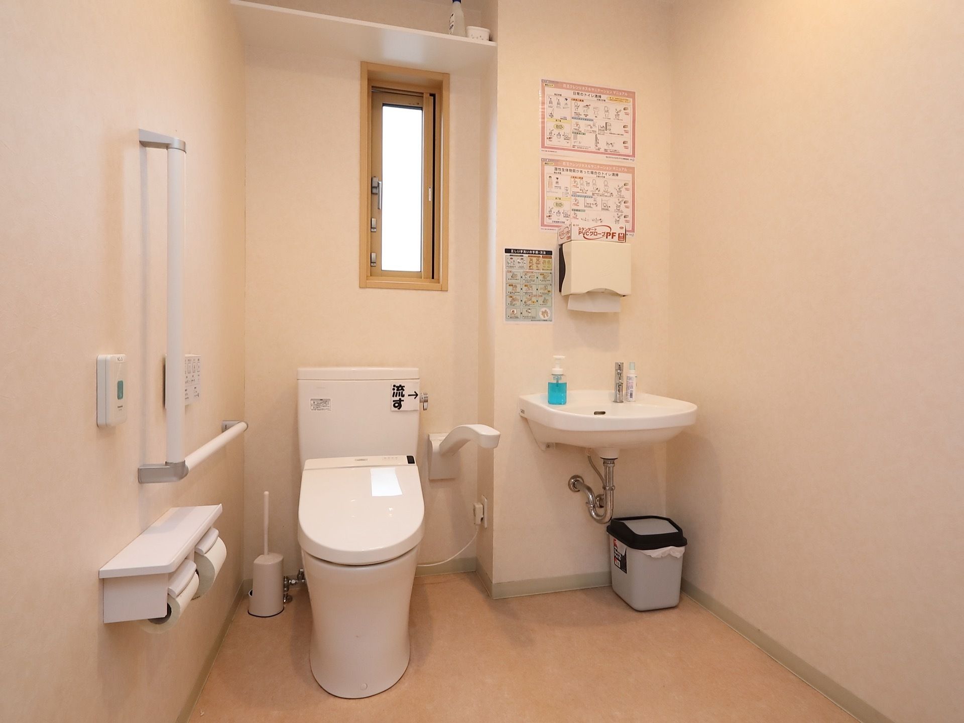 手すりや洗面台、温水洗浄便座が完備されたトイレである。壁には、呼出ボタンや備品を置く棚が設置されている。