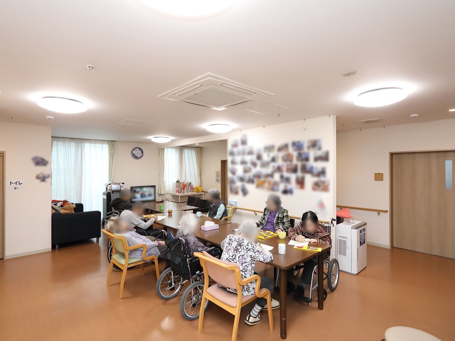 大きな一室に、入居者様が集まっている。テレビを観たり、お茶を飲んだりしながら過ごしている。壁には、イベントの写真を展示している。
