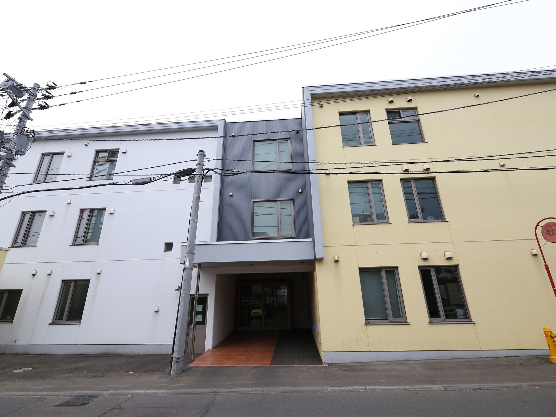 白、黒、クリーム色の三階建ての施設。段差がなく、車椅子をご利用の方も出入りしやすい設計となっている。