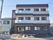 3階建ての建物の前には駐車場があり、看板も立っている。