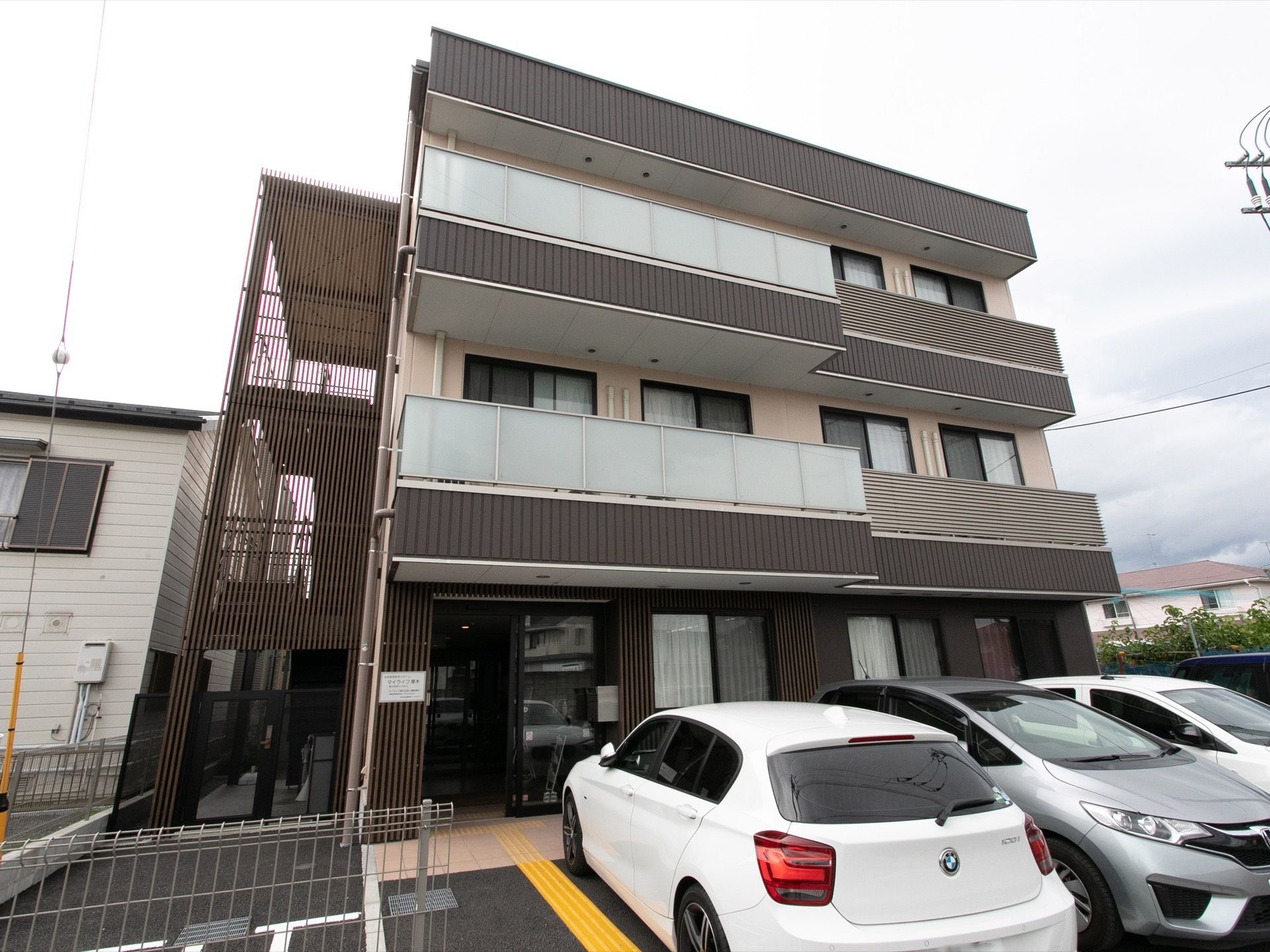 建物は3階建てで、2階と3階のベランダには半透明のプレートが設置されている。建物の前には駐車場があり、玄関へ続く道には点字ブロックがある。