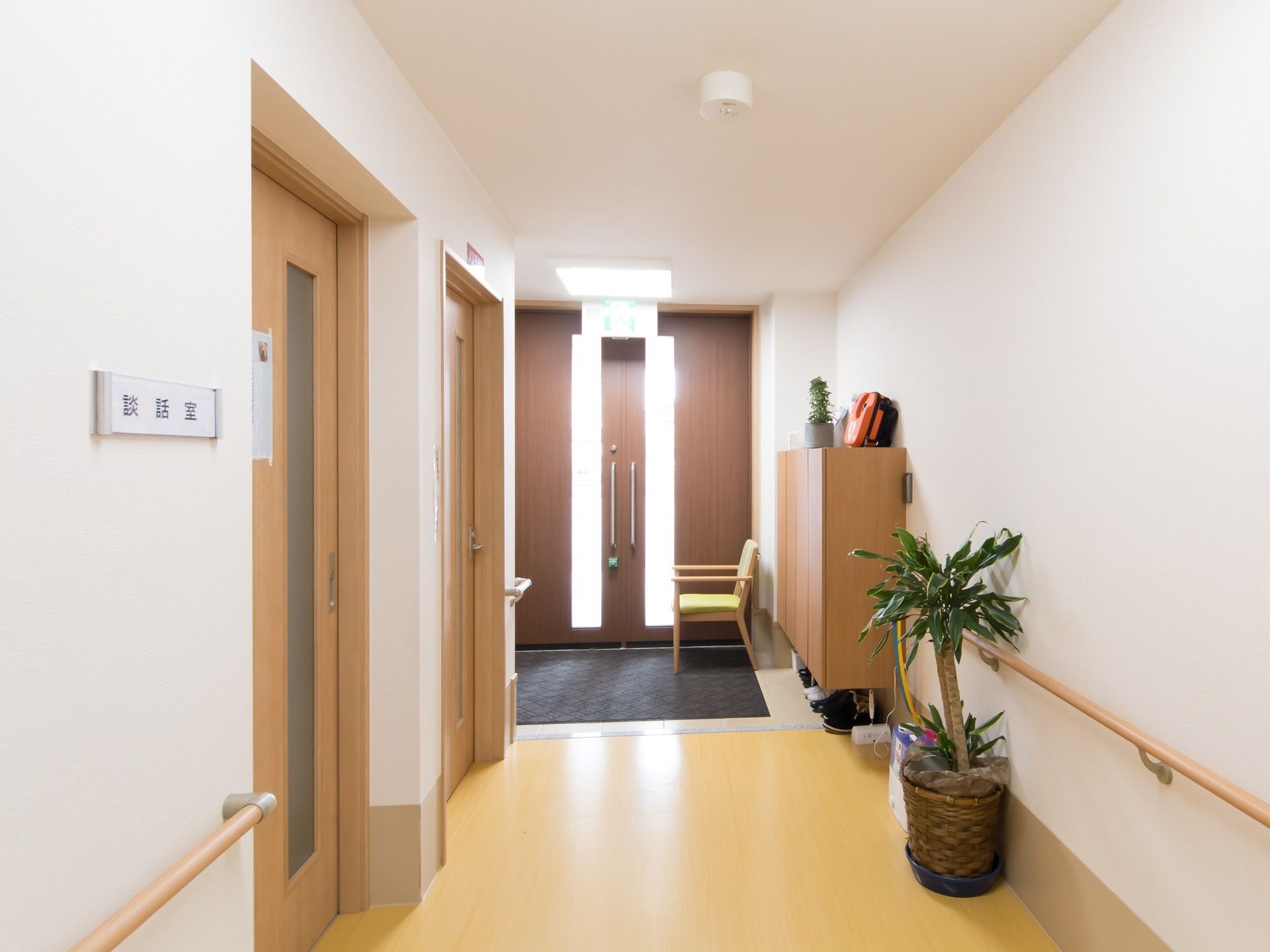 廊下の壁面には手すりが施されており、その傍らには観葉植物がある。左側の壁面には扉があり、談話室と表示されている。