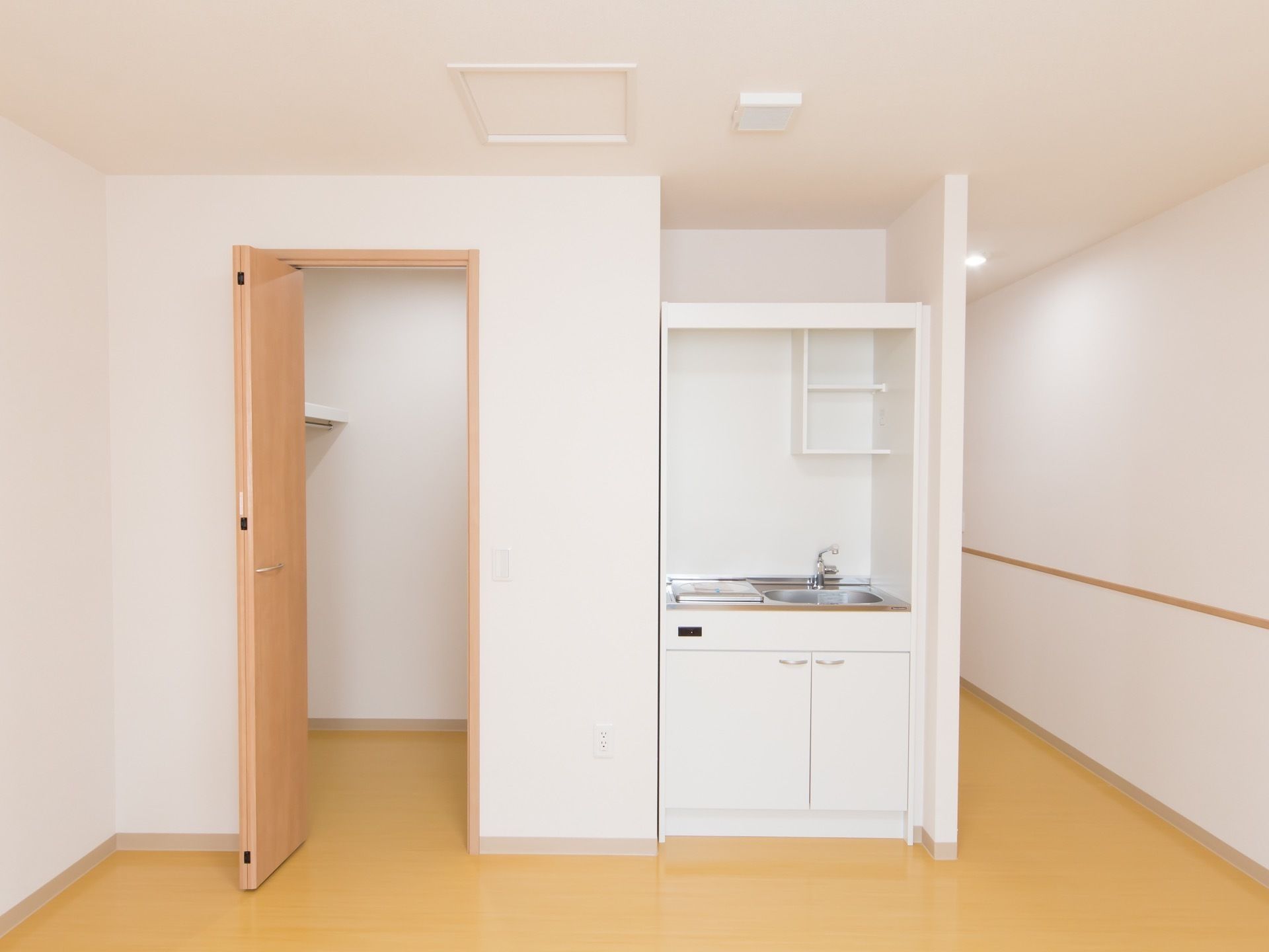 部屋の一角に小さな流し台がはめ込まれている。収納スペースの扉が開かれており、棚板やハンガーポールが見える。