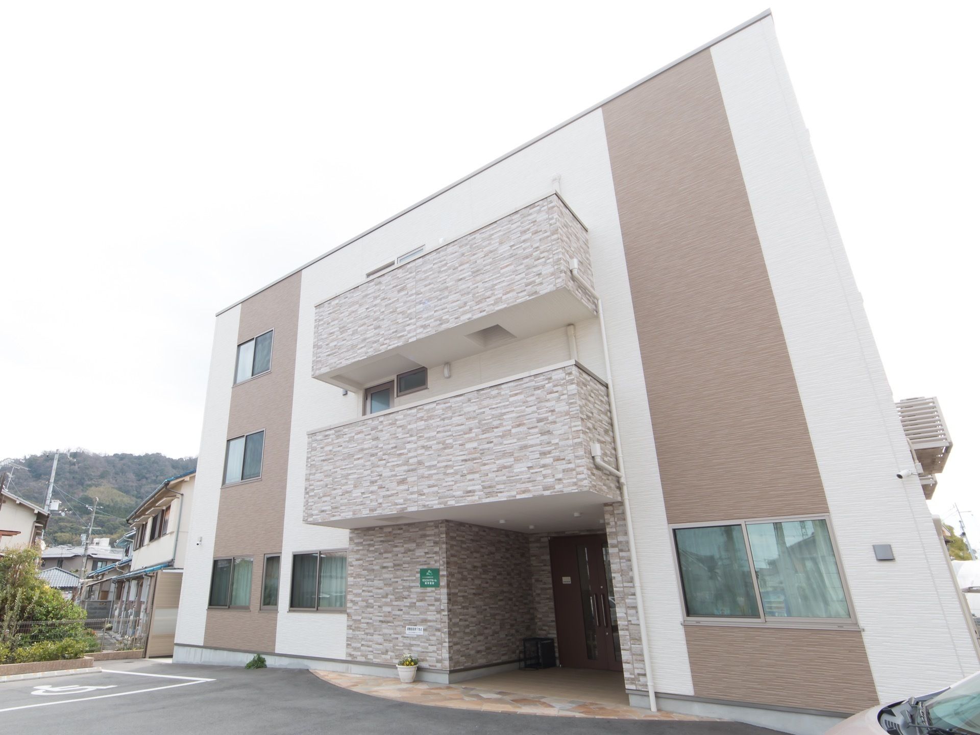 アスファルトで舗装された駐車スペースに囲まれて、3階建ての施設が建っている。淡い色調で統一され、さっぱりとしたデザインの建物である。