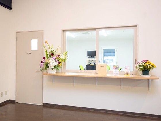 事務室には大きな受付の窓があり、両サイドには花が飾られている。左側にはスタッフが出入りするドアが付いている。