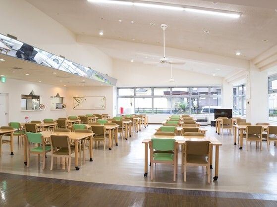 天井が高い広々とした食堂にはグリーンとブラウンの椅子がセットされた木製のダイニングテーブルがたくさん置かれている。