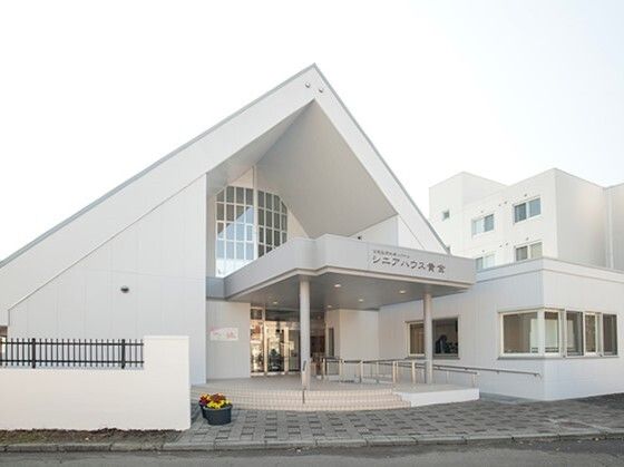 右側には三角屋根が付いた建物があり、右側には少し大きな建物があり、両方とも白。玄関には手すり付きのスロープもある。