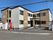 ベージュと白の2階建ての建物。玄関にはスロープと屋根も設置され、敷地内には駐車場もついている。
