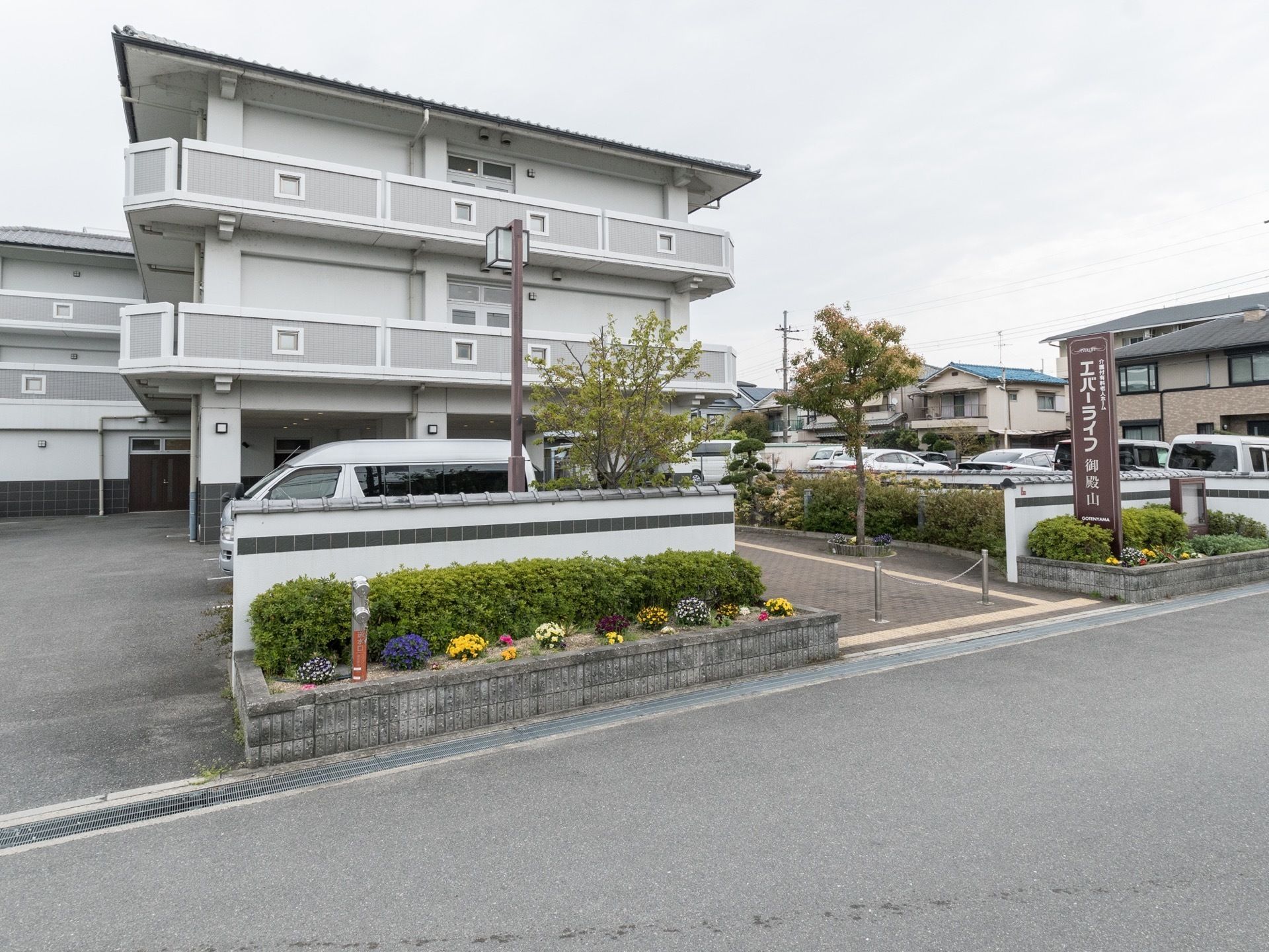 薄いグレーを基調とした外観の３階建ての建物である。道路に面した塀の傍に花壇を設け、縦長の看板を掲げている。