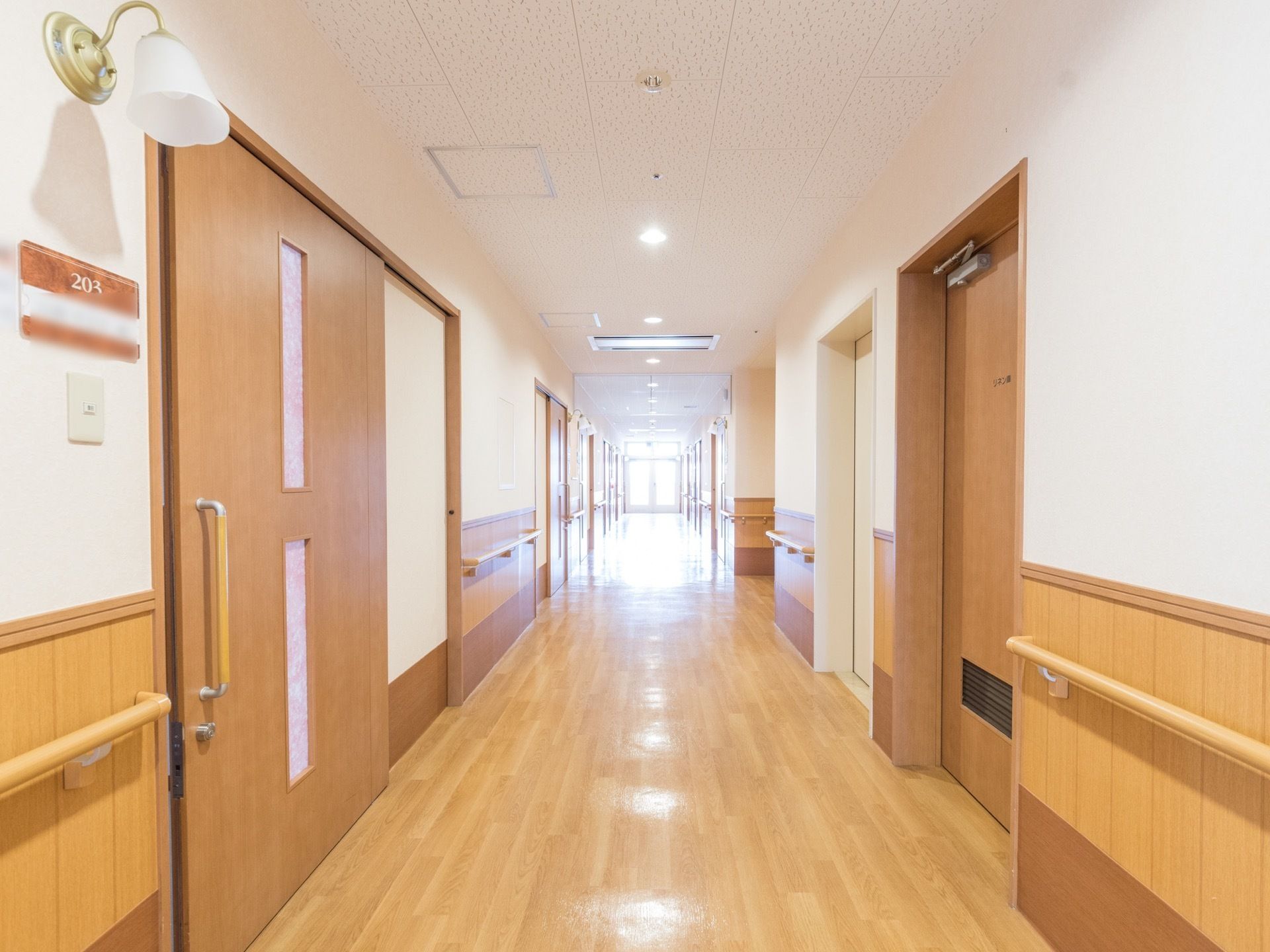 木目調を取入れた通路である。正面にガラス戸があり、明るい空間を確保している。壁に手すりを設置し、天井に間隔を置いて小さな円形の照明がある。
