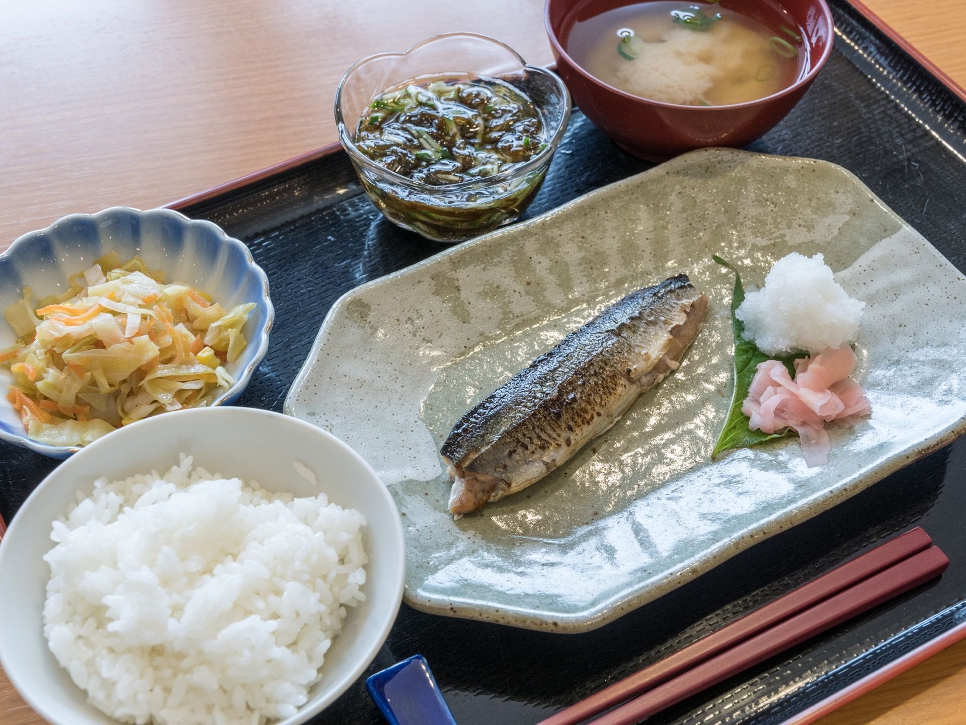 黒いトレーの上にご飯と汁物、メインおかずの焼き魚に、２つの小鉢を添えてセットした食事である。焼き魚は大根おろしで美味しくいただける。