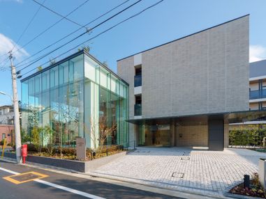 新01_広い式には桜の花が満開に割き、多くの緑が植えられている。ガラス張りの３階建ての建物。