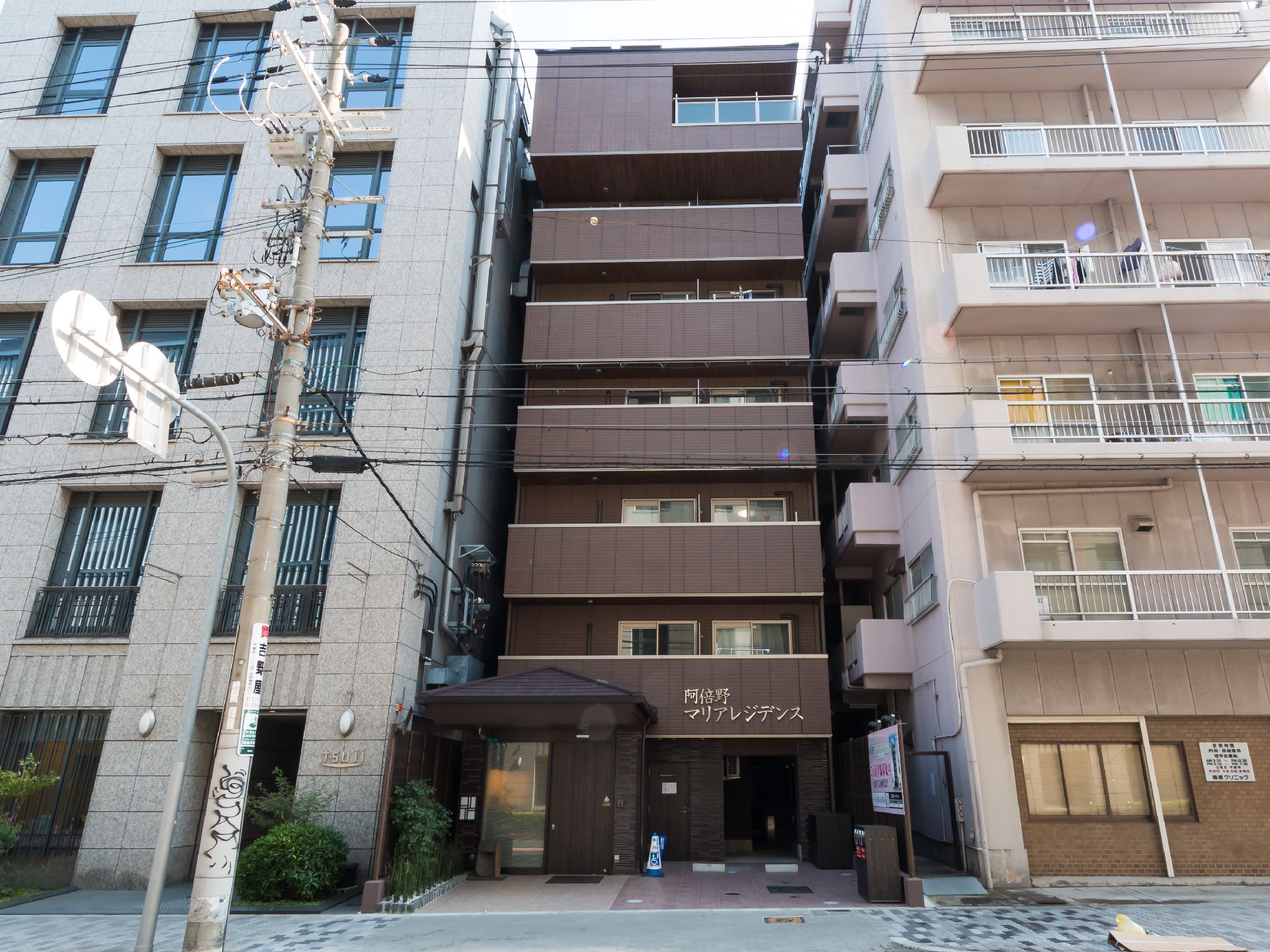 縦に長いブラウンを基調とした建物。７階建てで緑に囲まれている。