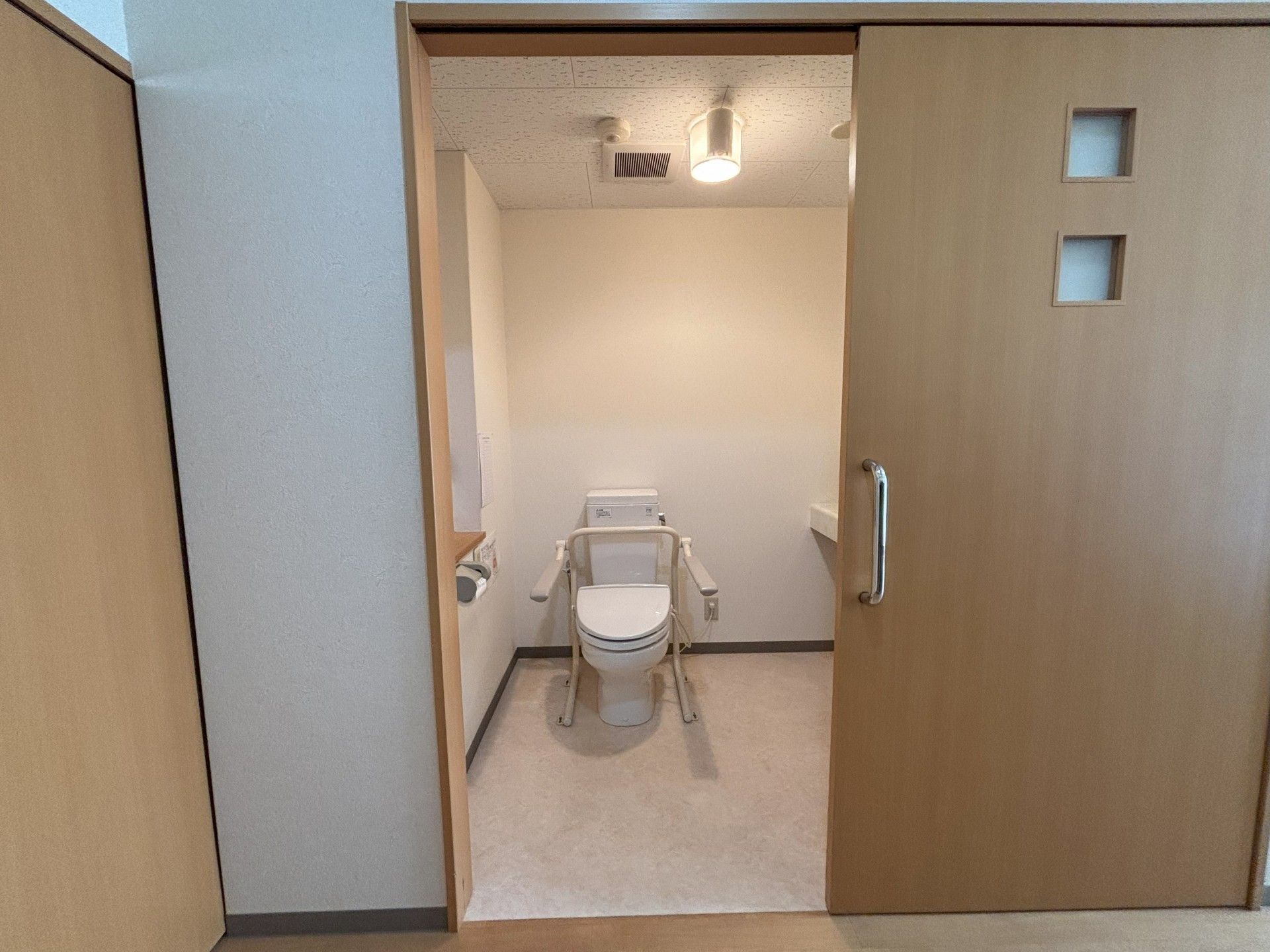 笑顔で遠方を指さしている車いすの高齢女性とそばで見ているエプロンを付けた女性スタッフ。