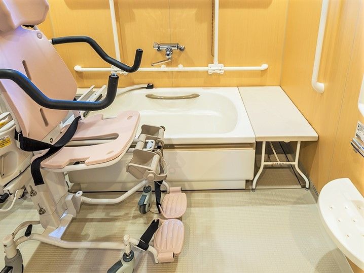 リフト浴。ピンクのリフトが置かれた個浴。リフトはピンクと白で、黒いベルトが付いている。