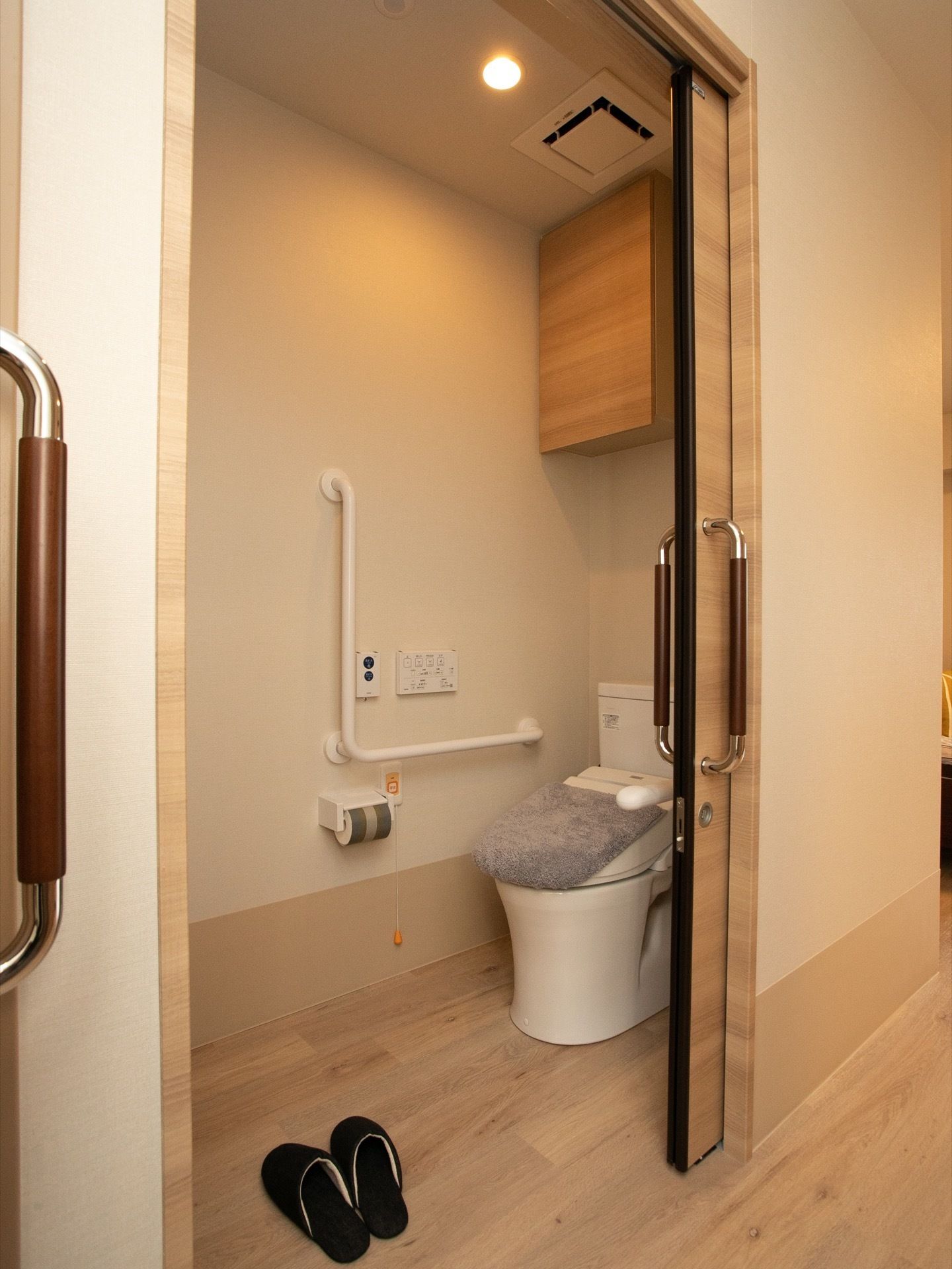 明るい色合いの木材を使用した、おしゃれなトイレである。扉は引き戸式仕様。黒色のスリッパが置かれている。