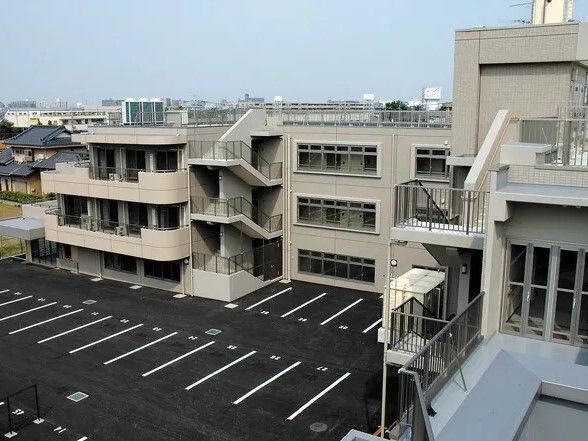 ベージュの外壁の3階建ての建物の各フロアにベランダがあり、屋外階段も設置され、駐車場も付いている。