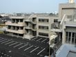 ベージュの外壁の3階建ての建物の各フロアにベランダがあり、屋外階段も設置され、駐車場も付いている。