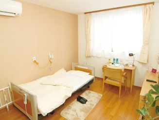 エアコンやカーテン付きの大きな窓が付いた居室はフローリングでベッドや観葉植物もある。