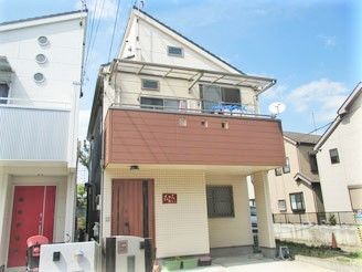 2階建ての茶色い建物。玄関には表札が付き、プランターも置かれている。