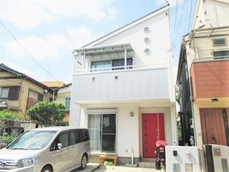 2階建ての白い建物にはベランダが付き、駐車スペースにはシルバーの車が止まっている。