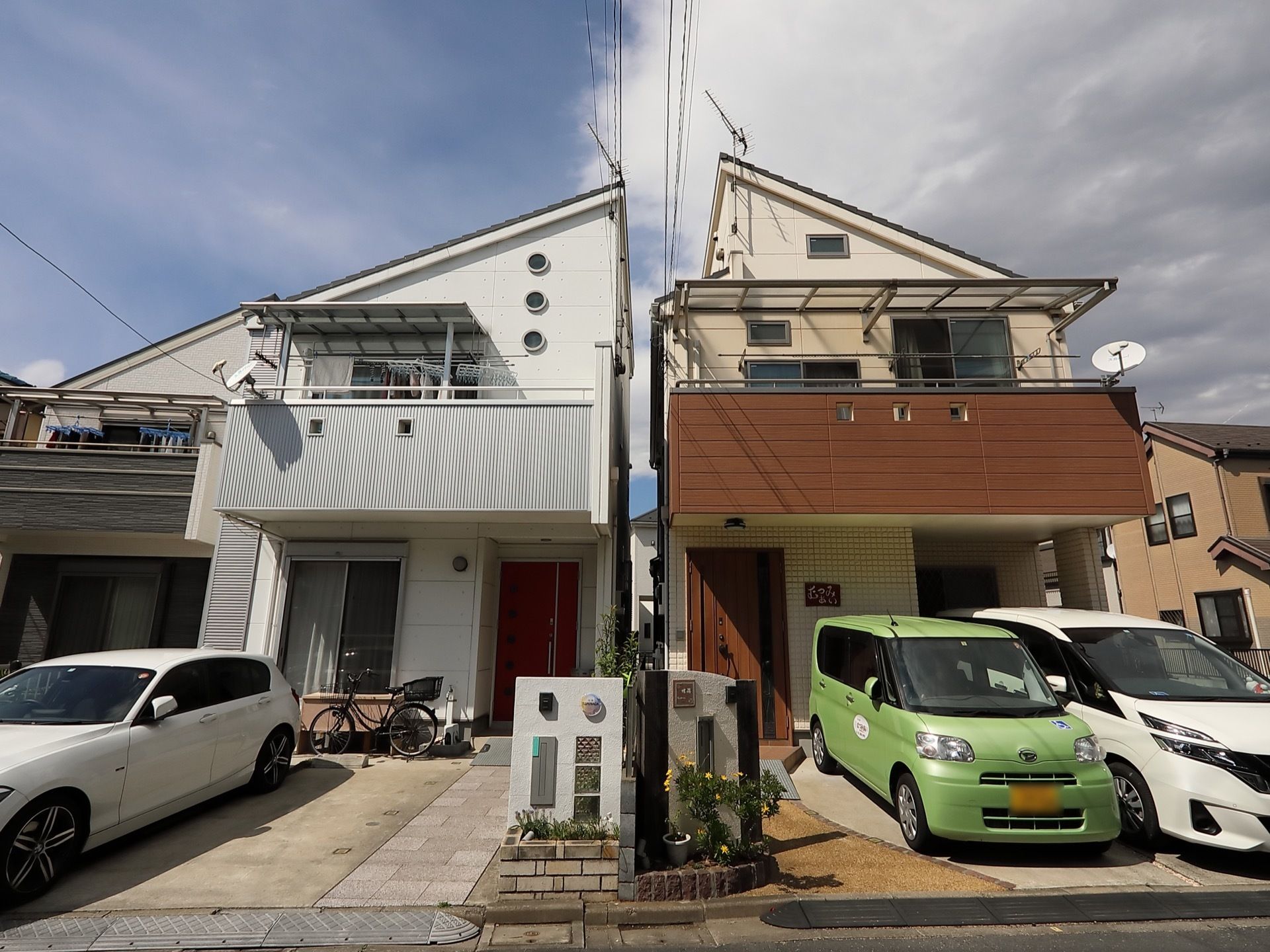 一軒家風の建物になっている。駐車場には車が停まっており、自転車も停められている。2階のベランダには洗濯物が干されている。