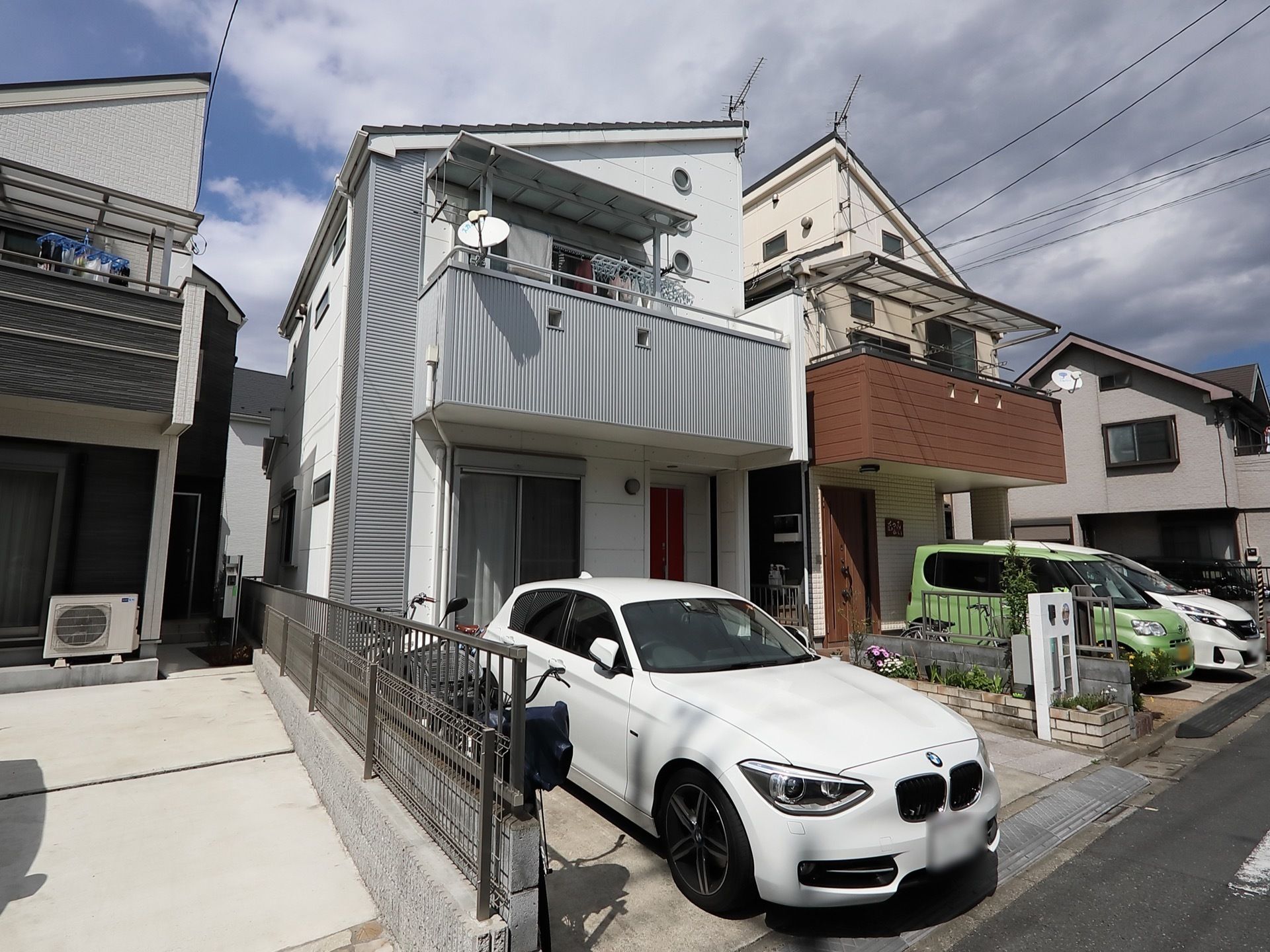 ２階建てのグレーの一軒家風の建物である。２階のベランダにはパラボラアンテナがあり、洗濯物が干されている。