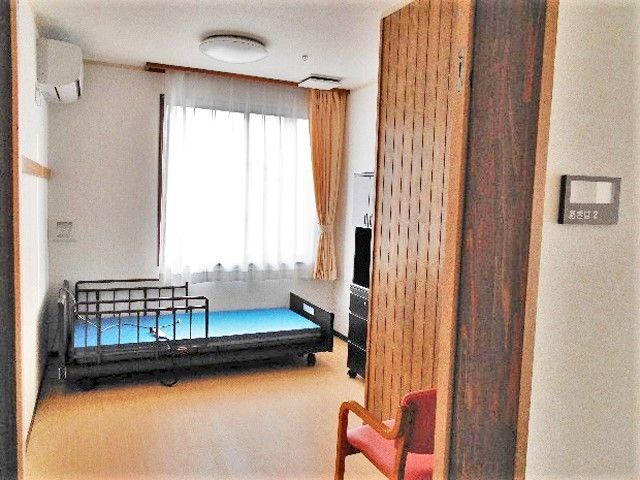 大きな窓が付いたフローリングの居室。エアコンとベッド、家具もある。