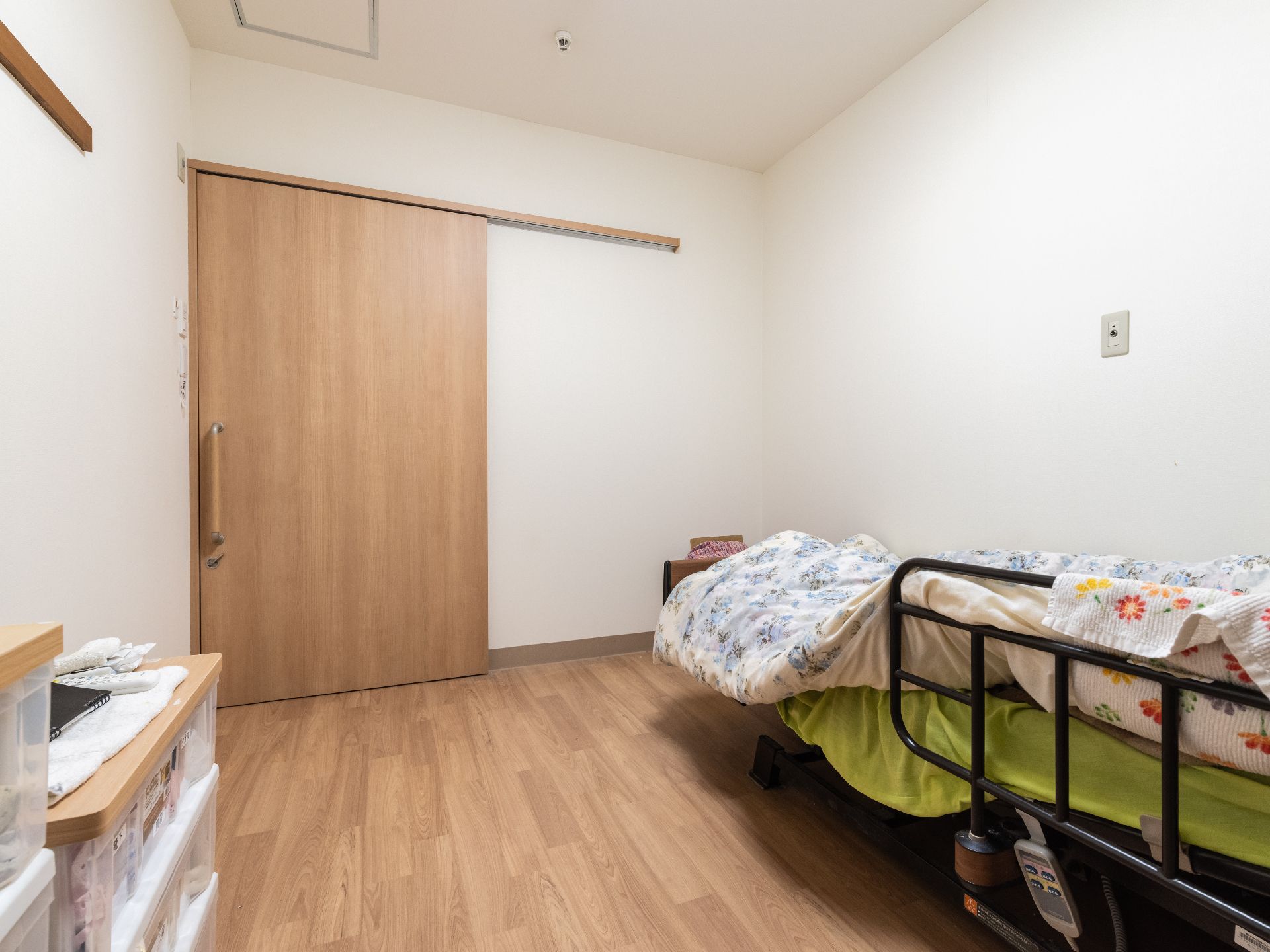 緑の多い屋外で笑顔で過ごしている車いすの高齢女性に付き添い、ピンクのエプロンを付けた若い女性スタッフが笑っている。