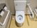 トイレには、手すりがある。床にごみ箱や掃除道具が置かれていて、壁にペーパーホルダーが設置されている。