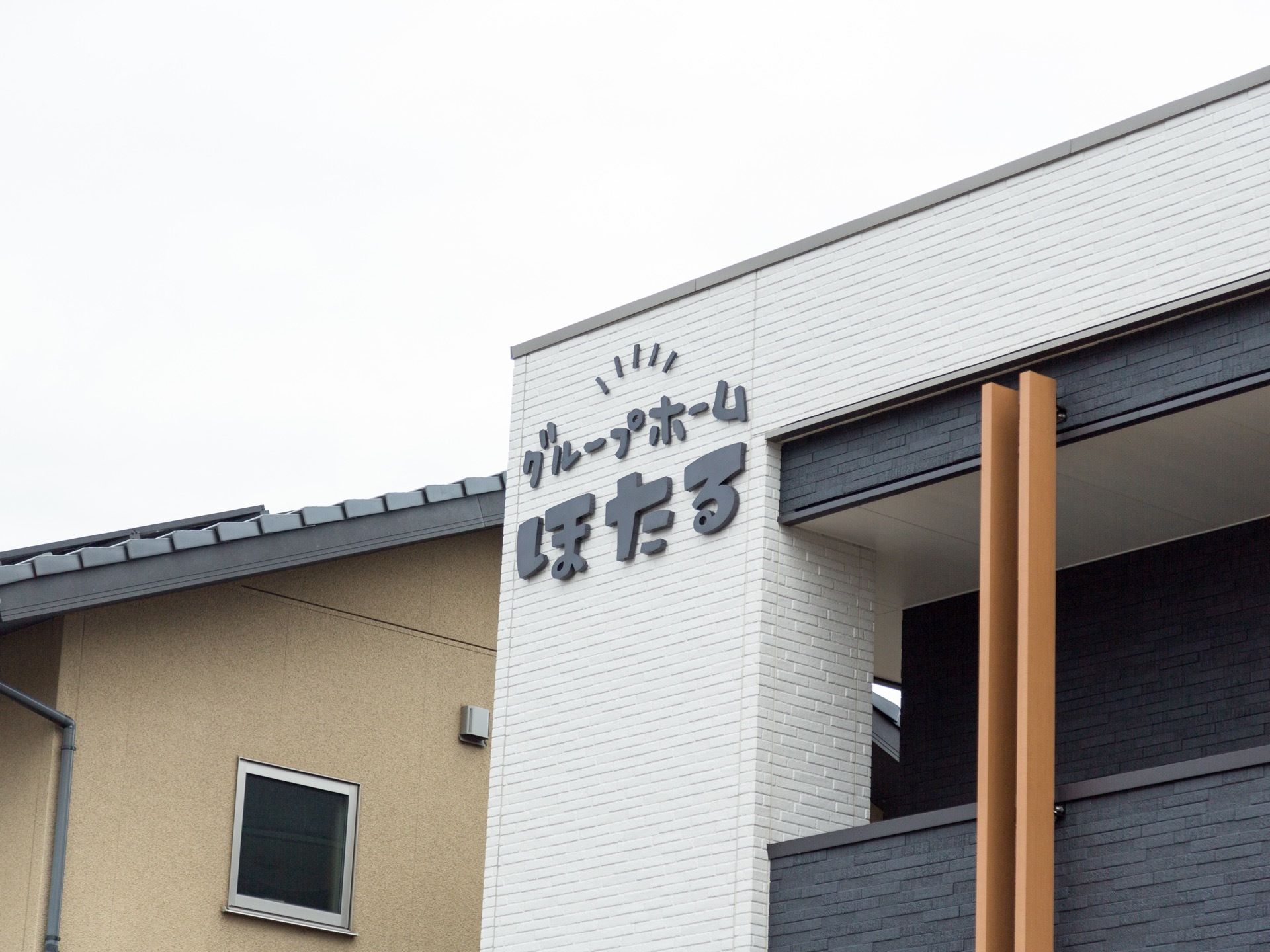 黒いタイルと白いタイルの部分があり、白いところには施設名の文字プレートが付けられている縦向きに、茶色い板が２本渡してある。