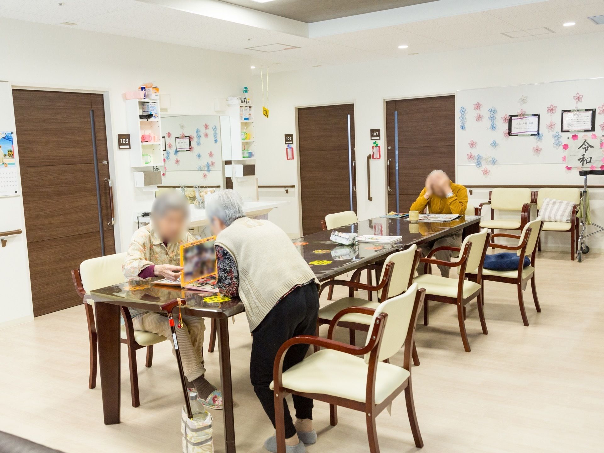 共有スペースでは入居者様が新聞を読んだり、談笑を楽しんだりして過ごしている。壁側には大きな洗面スペースがある。