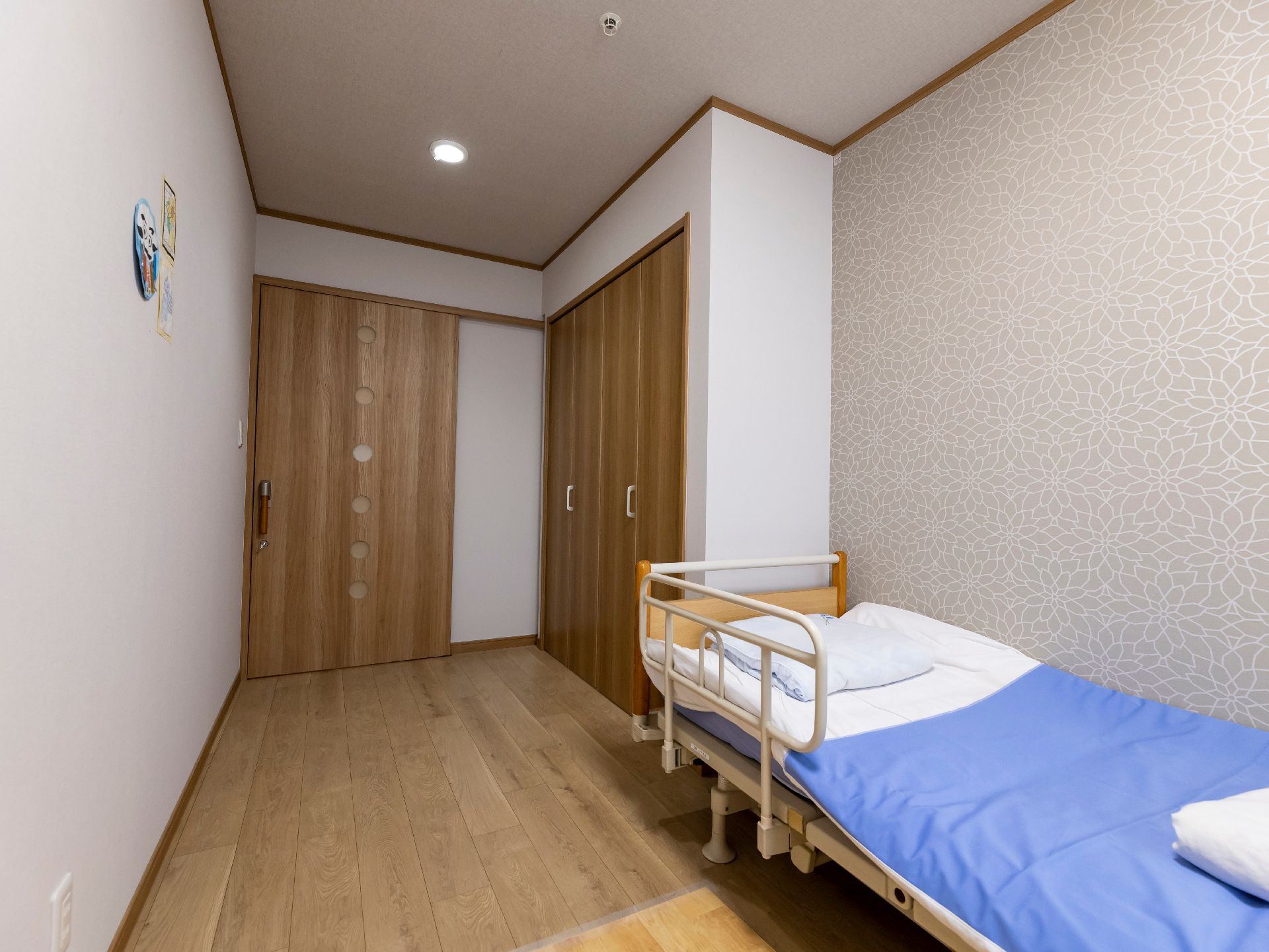 白いニット帽をかぶった車いすの高齢女性と付き添いの若い女性スタッフが屋外で過ごしている様子。スタッフはエプロンを付けている。