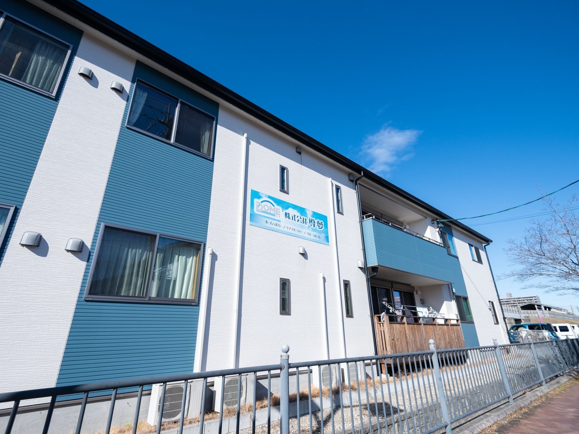 ベランダを完備した2階建ての施設である。白い外壁部分には、施設名称の入ったプレートが設置されている。