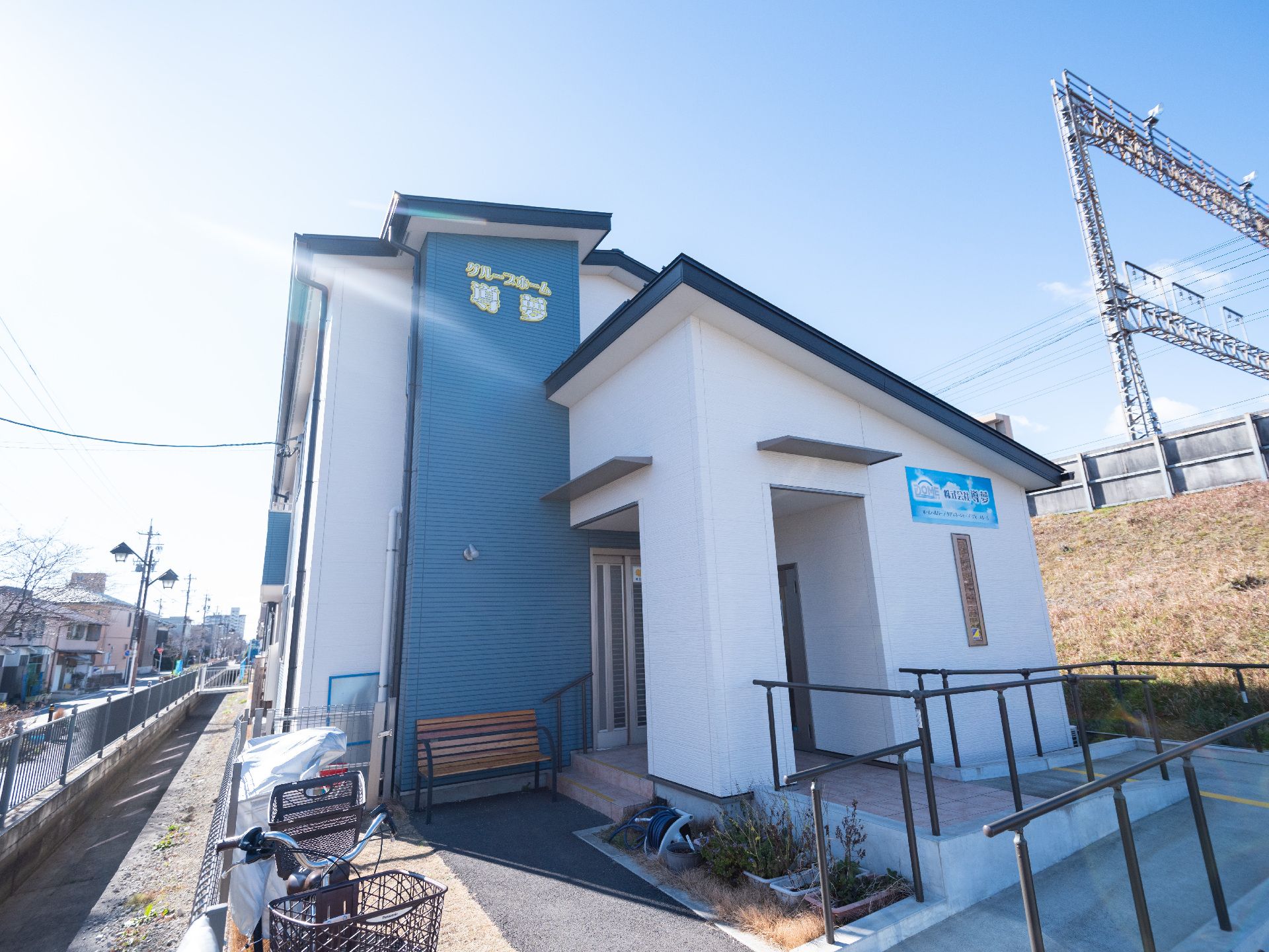 ２階建ての建物で、白色と青色の塗装でスロープや階段には手すりがある外観