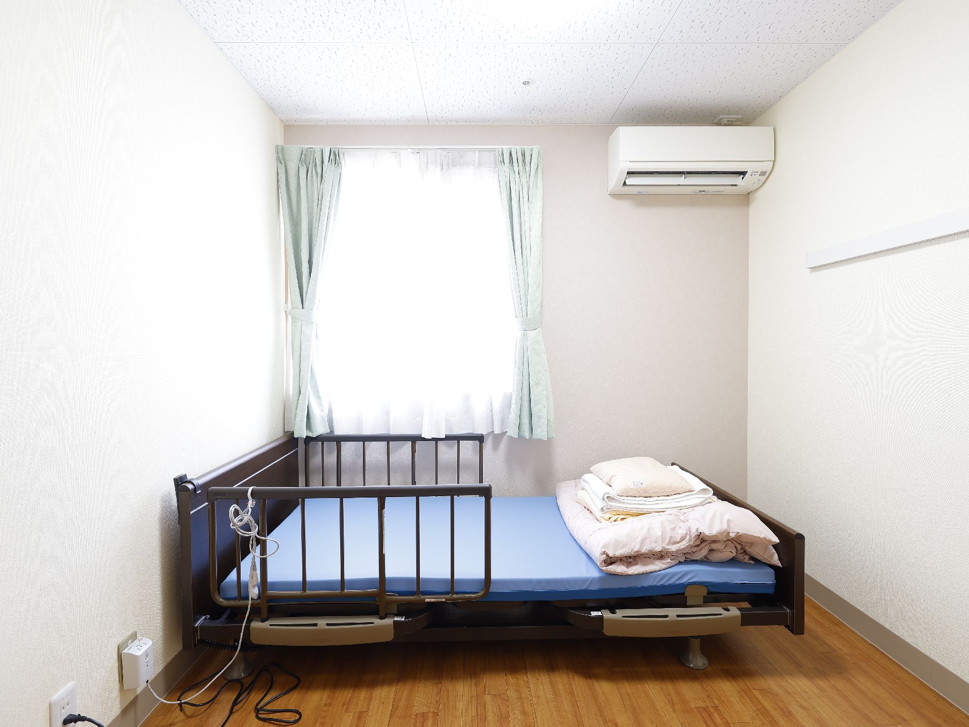 窓から陽光が入り、介護ベッド、エアコンが設置されている居室