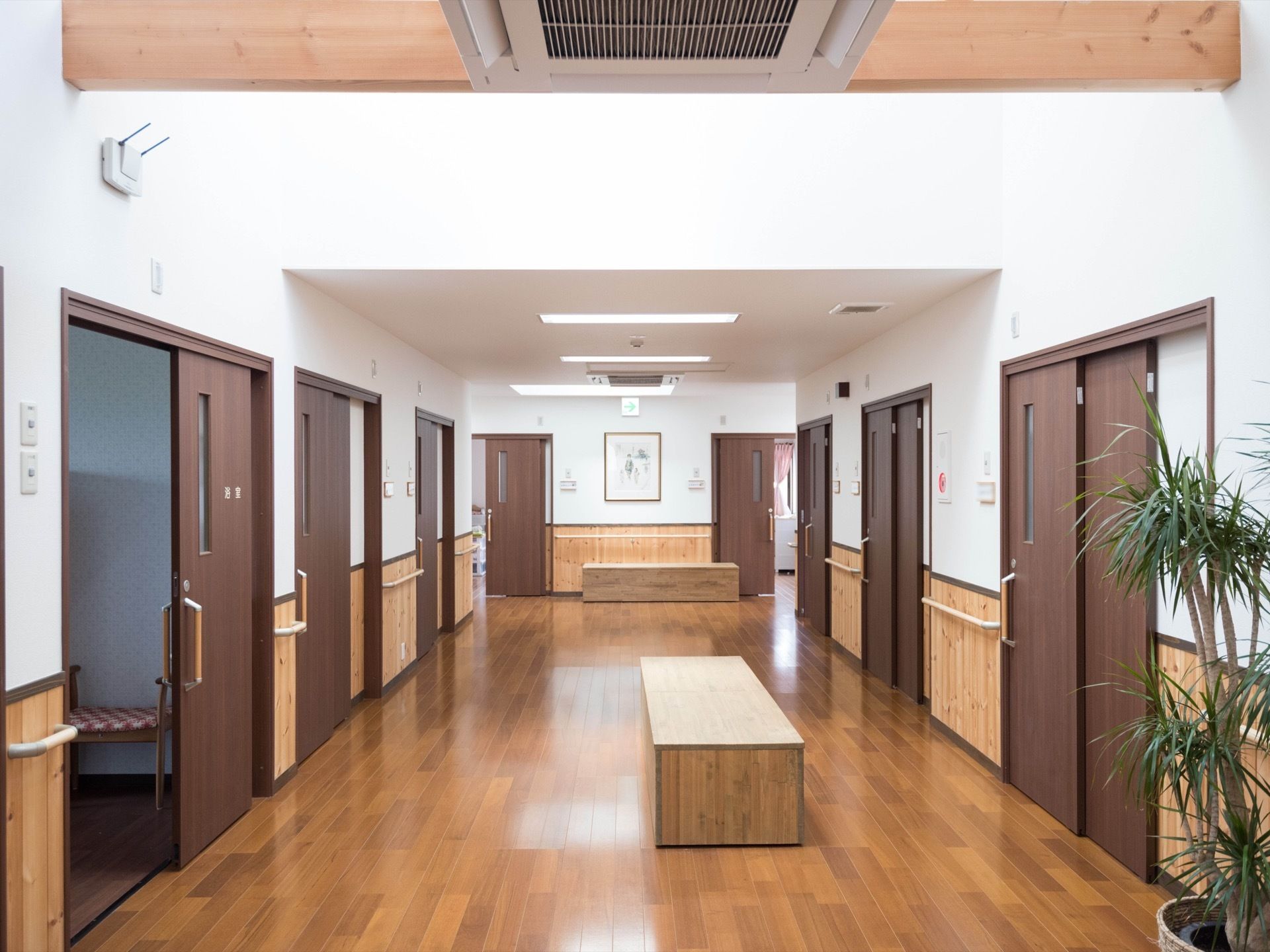ゆったりとした広さの廊下である。両側は居室のドアが並んでいる。真ん中にはベンチが置かれ、腰掛けることができる。