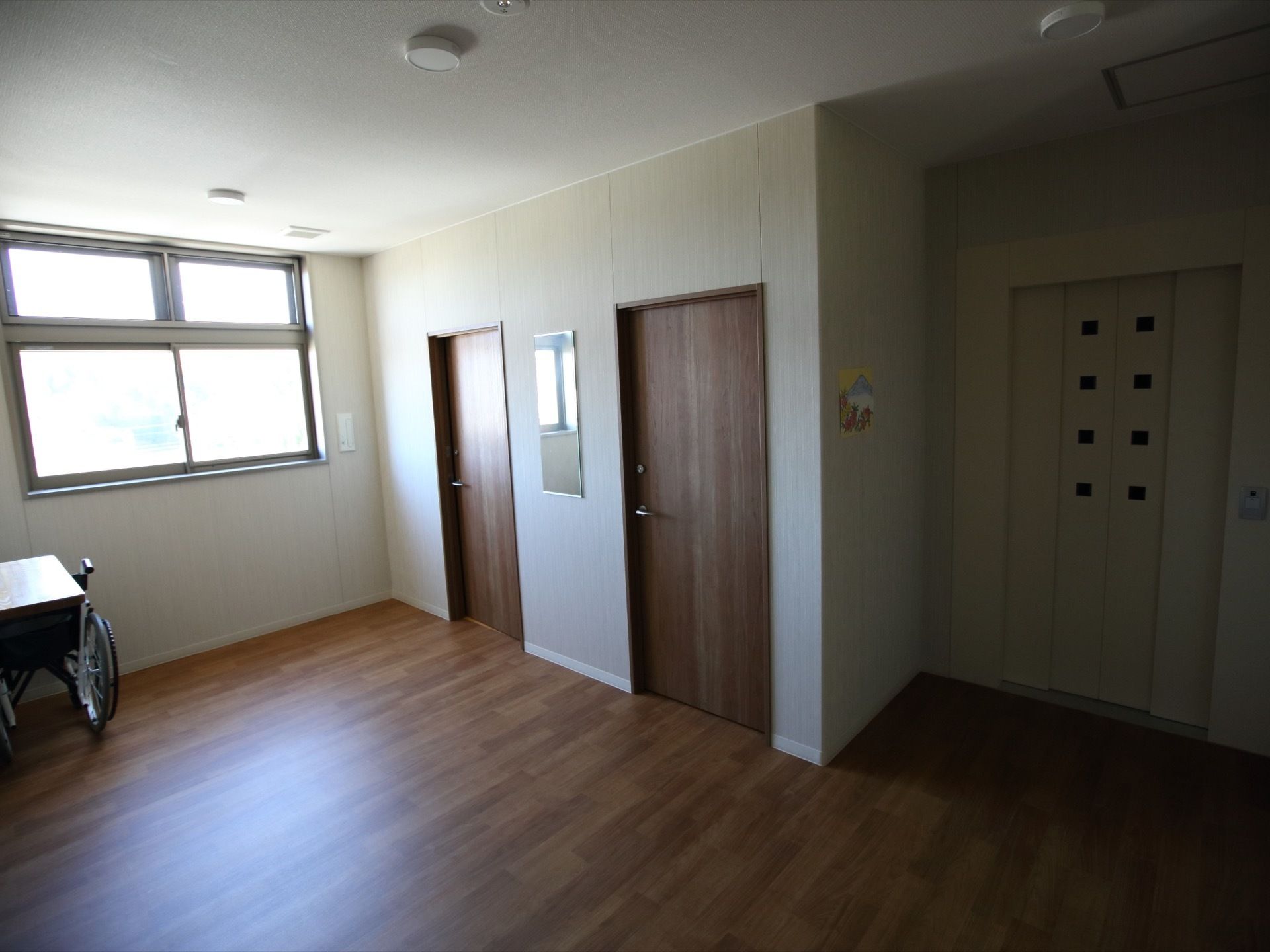小窓が付いた扉のエレベーターと部屋のドアが並ぶホールである。障害物はなく、広々とした空間となっている。