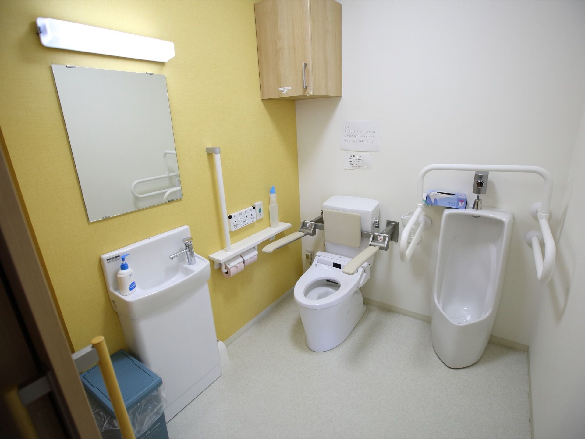 白い空間に黄色のアクセントクロスを貼ったトイレスペースである。温水洗浄便座のほかに、手洗い場や男性用便器も設けている。