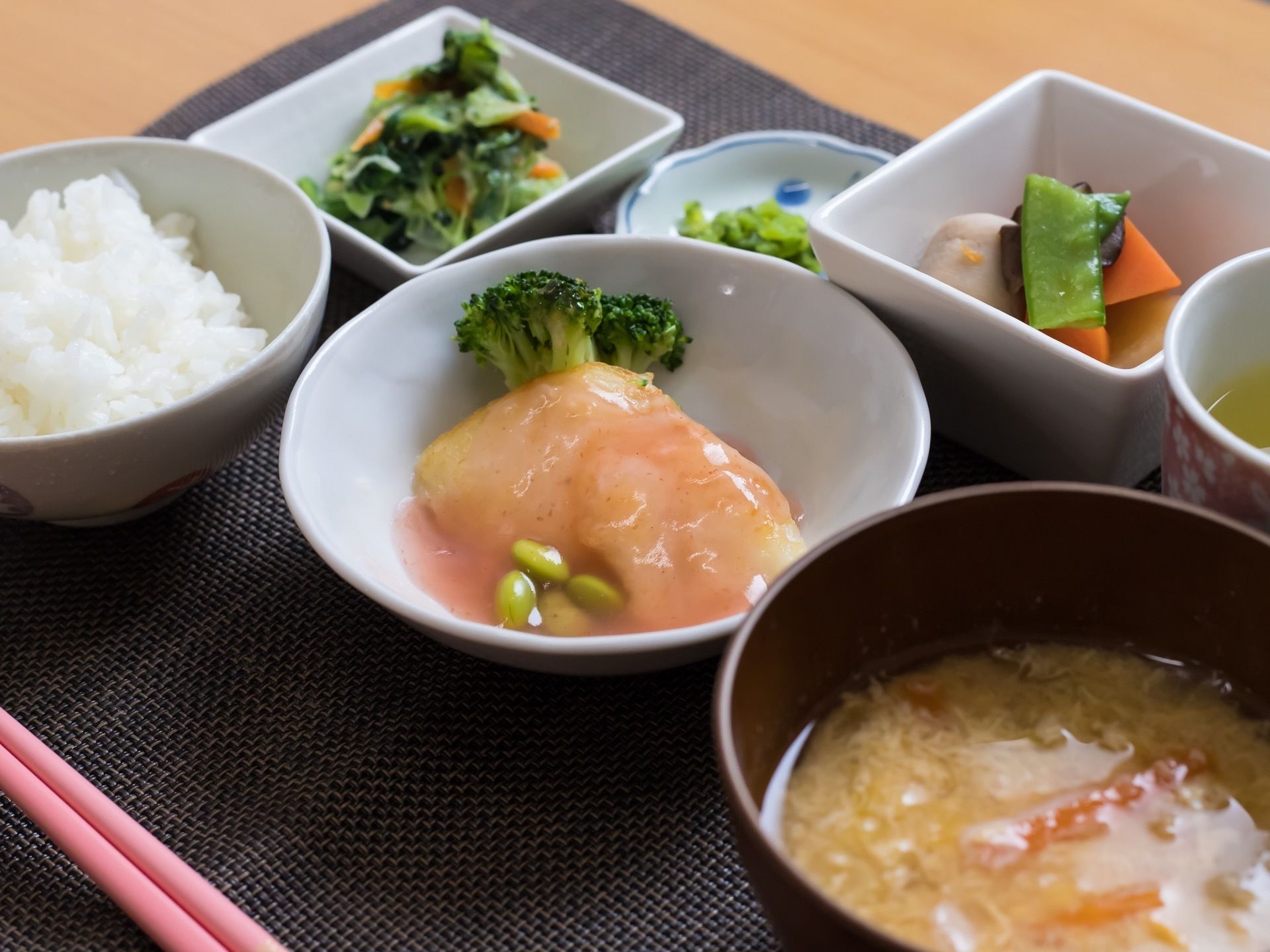 黒系のランチョンマットの上に置かれた食事がある。ごはんと汁物、小鉢が３皿、お新香の小皿とお茶がある。