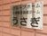 赤茶色のタイルが貼られた建物の外壁がある。金属のプレートに、黒い文字で施設名が書かれており、四隅を鋲で留められている。