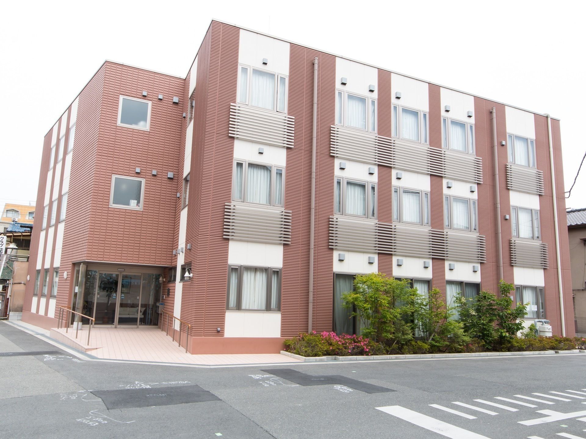 ブラウン系でまとめられたどっしりとした建物の周りには駐車場があり、緑も植えられている。
