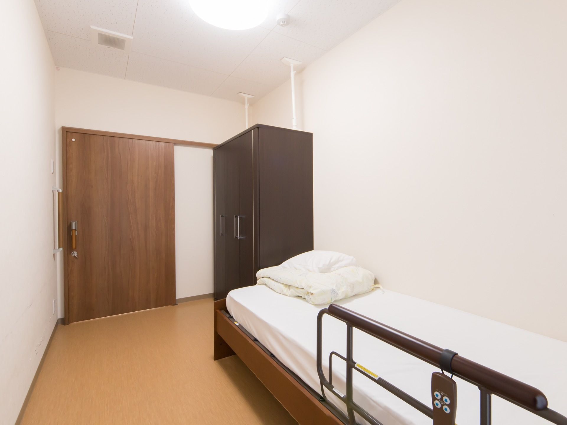大きな木製の引戸で出入りする居室である。フローリングの洋室で、柵付きのベッドが置かれている。大きな収納家具があり、衣類などを収納できる。