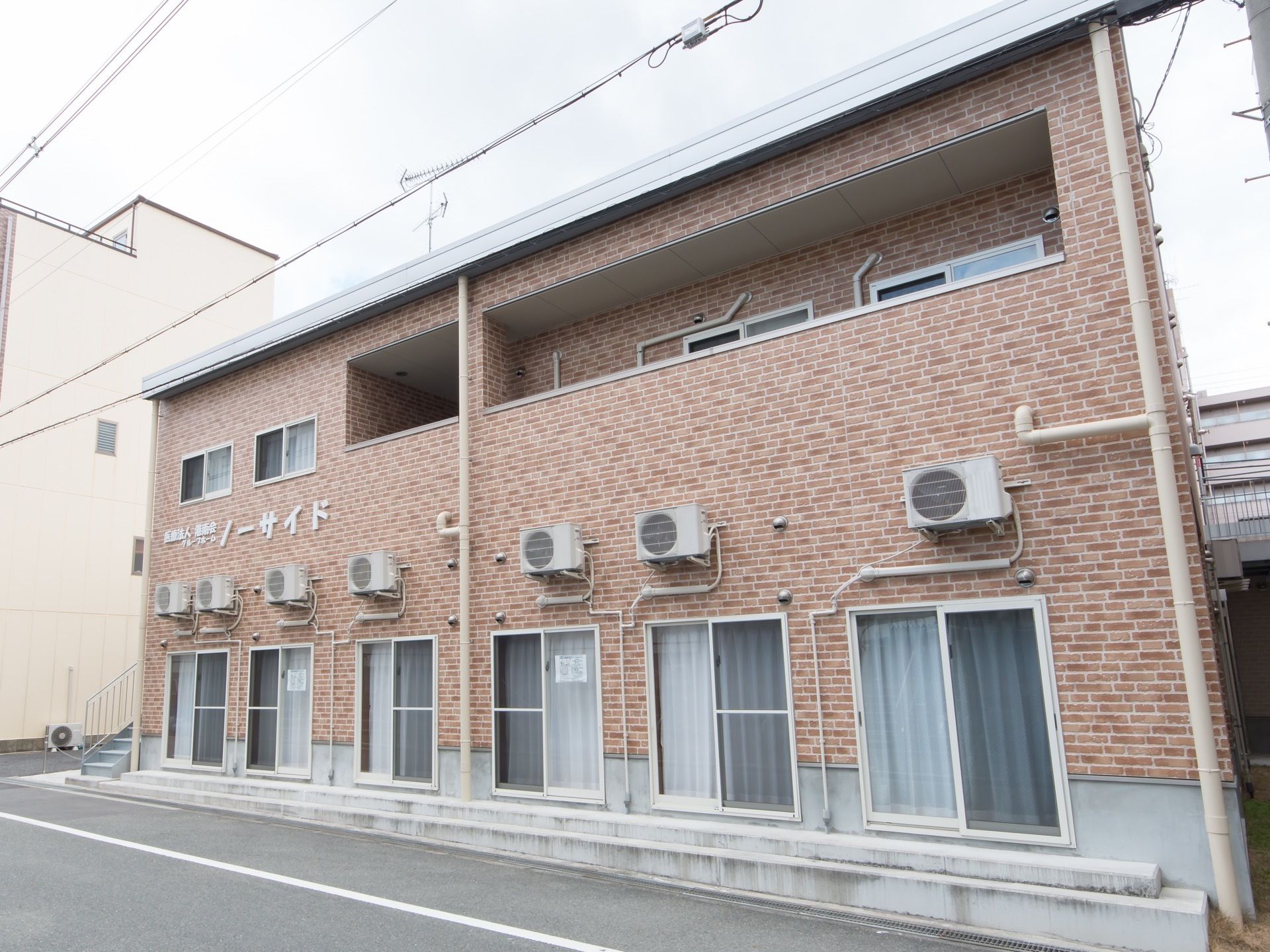 住宅地にある施設は、レンガタイルの外壁で、施設名が大きく表記されている。窓と室外機が並んだ２階建だ。