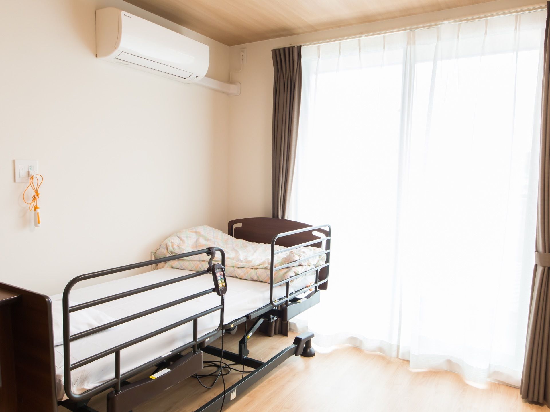 明るい部屋にサイドレールのついた介護ベッドが置かれている。壁にはナースコールやエアコンが設置されている。